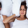 Woman blocking ears while man snoring on bed